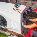 An Air Conditioning Technician Wearing a Red Shirt and Hat Works on an Outdoor System.