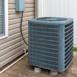 An Air Conditioning Condenser Installed Outside of a Grey House.