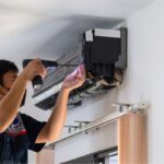 An Ac Technician in Blue Coveralls Uses a Drill to Install an Air Conditioner.