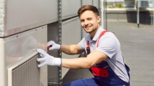 An HVAC technician wearing a white polo shirt smiles.
