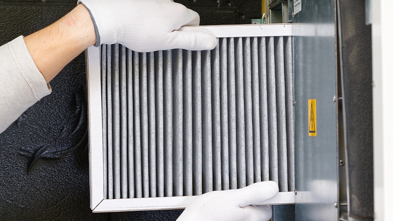 Gloved hands remove the filter from an HVAC unit.