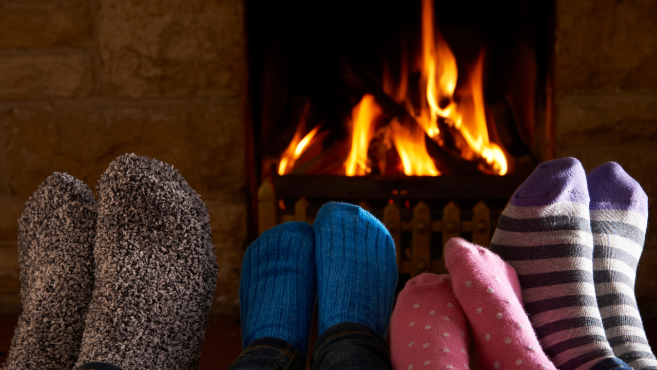 A family warms their feet by a roaring fireplace in their home.